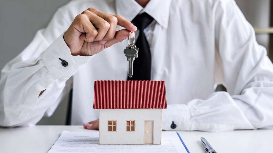 a person holding house keys over a home figurine